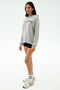 A woman wears the SPLITS59 Andie Oversized Fleece Varsity Graphic Sweatshirt in heather grey with "Los Angeles" text, paired with black shorts, white socks, and sneakers, standing against a plain white background.