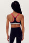 A person wearing a SPLITS59 Bianca Rigor Bra - Black with pink straps and matching black leggings made of stretchy spandex fabric is shown from the back.