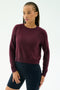 A person with braided hair wears the SPLITS59 Brooks Fleece Long Sleeve Sweatshirt in Dark Cherry and black shorts, standing against a plain white background.