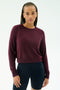 A person with braided hair wears the SPLITS59 Brooks Fleece Long Sleeve Sweatshirt in Dark Cherry and black fitted modal spandex shorts, standing against a plain white background.