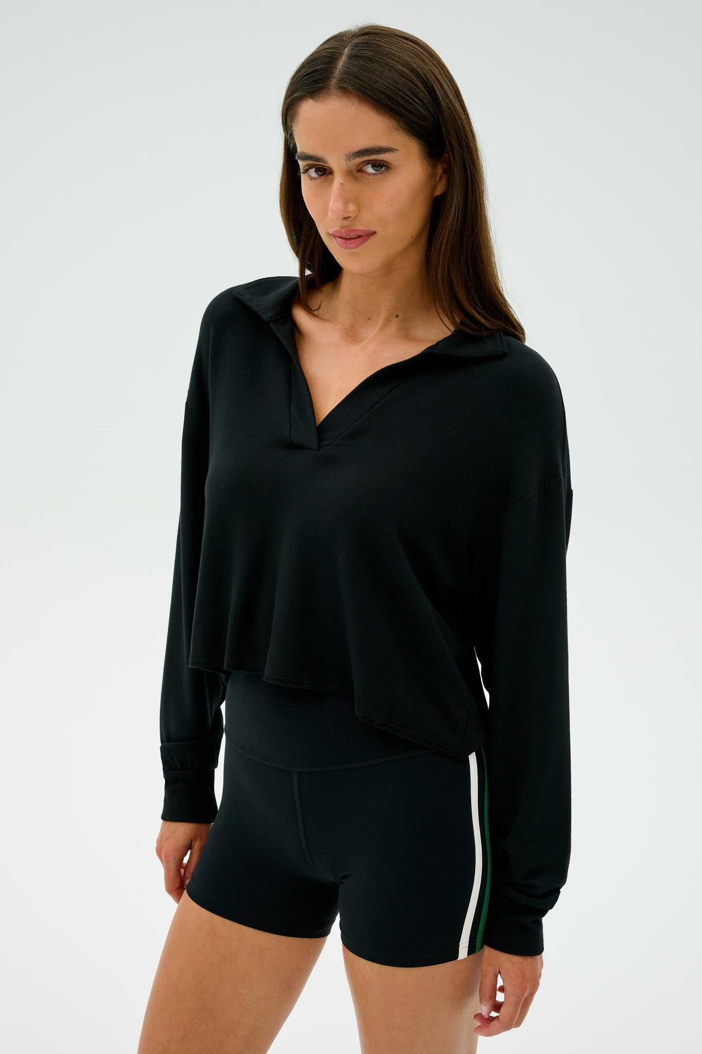A person wearing the SPLITS59 Joan Fleece Polo Sweatshirt in black and black shorts with white stripes stands against a plain background.
