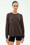 A woman wears the SPLITS59 Andie Oversized Fleece Sweatshirt in Dark Chocolate with black shorts, standing against a plain white background.