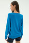 Woman wears the SPLITS59 Bennie Fleece V-Neck Sweatshirt in Stone Blue with black shorts, facing away from the camera against a plain light background.