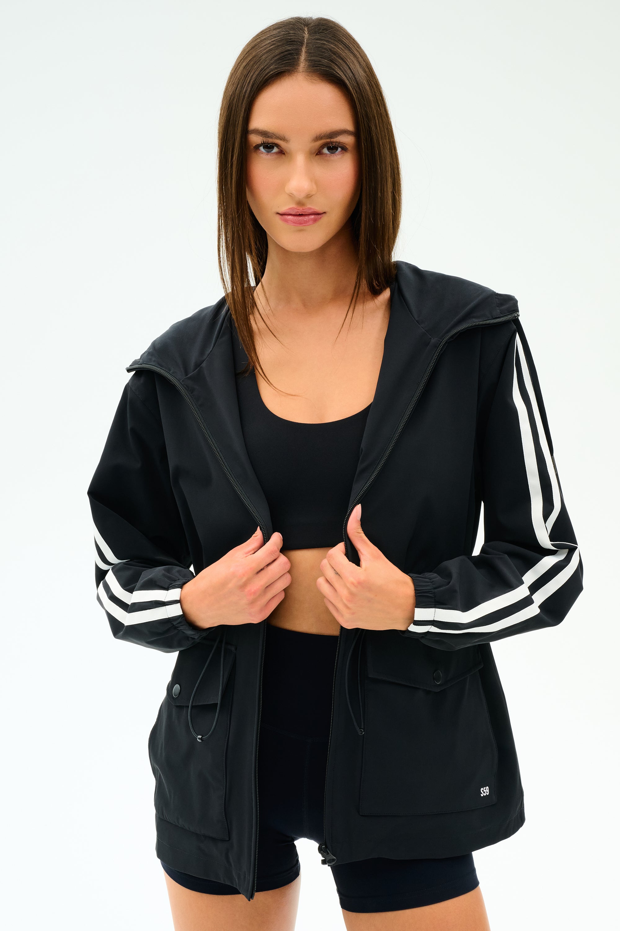 A woman stands against a white background wearing the SPLITS59 Reggie Water Repellent Jacket in black/white.