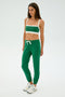 A person in green SPLITS59 Sonja Fleece Sweatpant in Arugula, a green and white sports bra, and white sneakers stands on a plain background.