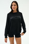 A woman wears the SPLITS59 Andie Oversized Fleece Varsity Graphic Sweatshirt in black with "LOS ANGELES" text, paired with matching black shorts, standing against a plain light background.