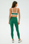 An individual in SPLITS59's Clare High Waist Rigor 7/8 leggings and a green sports bra, made from high-performance Rigor fabric, stands facing away on a plain white background.