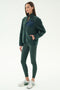 A woman wears the SPLITS59 Harris Sherpa Jacket in Military/Indigo, paired with dark green leggings and white sneakers, standing against a plain light background.