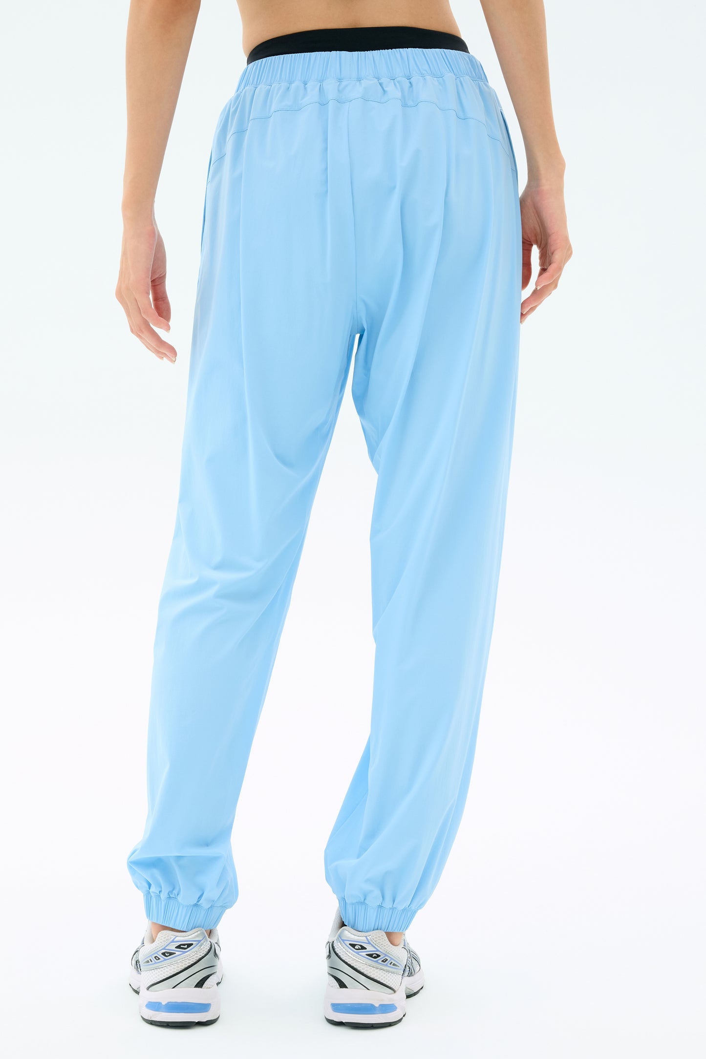 A person wearing SPLITS59 Megan Woven Nylon Jogger in Skylight and white sneakers, photographed from the back against a plain white background.