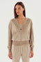 A woman wearing a SPLITS59 Rhys Velour Zip Up Hoodie - Latte over a matching top and pants stands against a plain white background, showcasing the comfort and versatility of her post-workout clothing.