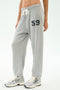 Model wears SPLITS59 Andie Oversized Fleece Varsity 59 Sweatpant in Heather Grey with a "59" graphic on the left thigh and white sneakers—ideal for cool weather workouts, posed against a plain background.