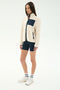 A woman wears the SPLITS59 Harris Sherpa Jacket in Creme/Indigo, styled with navy bike shorts, white socks, and white sneakers, standing against a plain light background.
