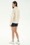 Woman wearing the SPLITS59 Harris Sherpa Jacket in Creme/Indigo, paired with navy blue shorts, white socks, and white sneakers, stands against a white background facing slightly away from the camera.