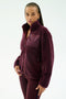 A person wears the SPLITS59 Harris Sherpa Jacket in Dark Cherry—a soft polyester fleece zip-up with a chest pocket—paired with matching leggings, standing against a plain light background.