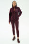 A woman wears the SPLITS59 Harris Sherpa Jacket in Dark Cherry, styled with matching leggings and sneakers, standing against a plain white background.
