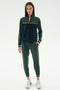A woman faces forward in the SPLITS59 Millie Airweight Half Zip in Military/Indigo, a soft nylon tracksuit with a front zip, paired with white sneakers, against a plain white background.