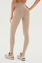 A person wearing beige high-waisted SPLITS59 Airweight Super High Waist 7/8 - Latte leggings, crafted from ultra luxe Airweight fabric, and light-colored sneakers stands against a white background, facing away.