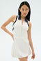 A woman models the SPLITS59 Austin Rigor Dress in white/indigo, a sleeveless tennis dress, against a plain light background.