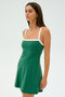A woman in the Monah Rigor Dress from SPLITS59, featuring an arugula-green color with white straps, stands against a plain background, facing slightly to the left.