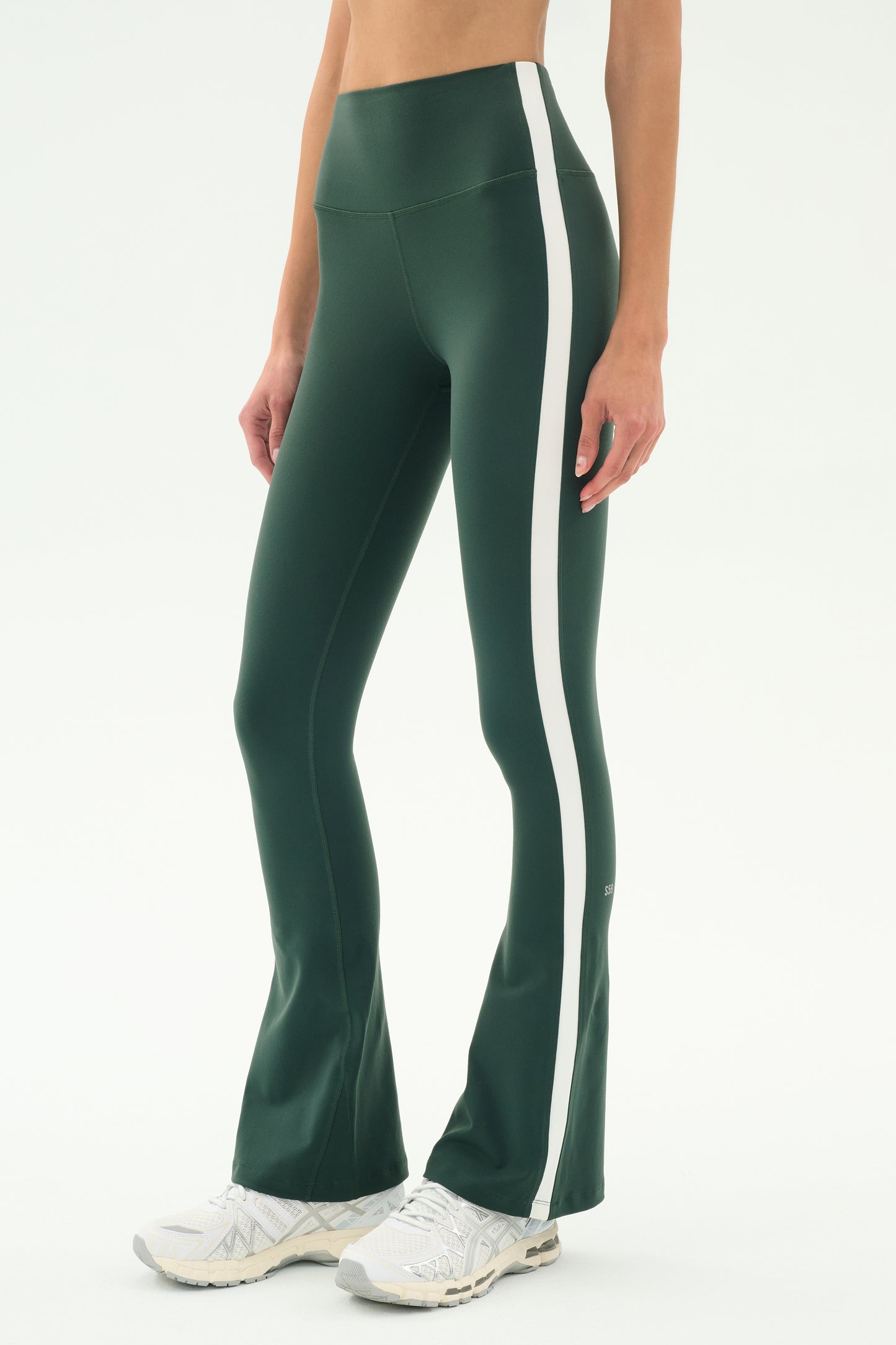A person wearing SPLITS59's Raquel High Waist Flared Legging in Military/White and white sneakers stands against a plain background.