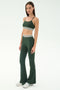 A woman stands against a plain background wearing the SPLITS59 Cali Active Rib Bra in Heather Military, paired with matching high-waisted flared leggings featuring white stripes and silver sneakers.