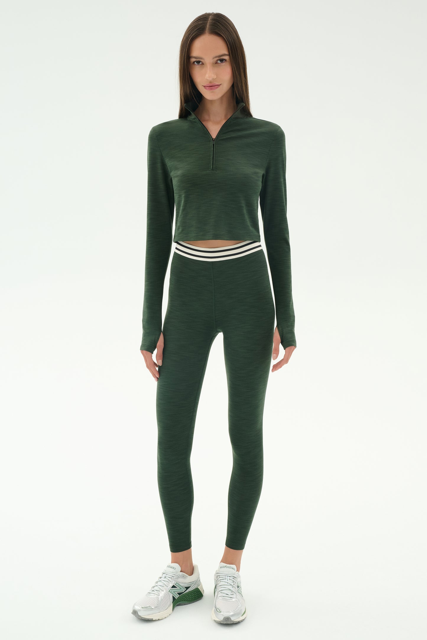 A person faces forward wearing the SPLITS59 Stevie Active Rib Half Zip in Heather Military, paired with matching high-waisted leggings and white sneakers, against a plain white background.