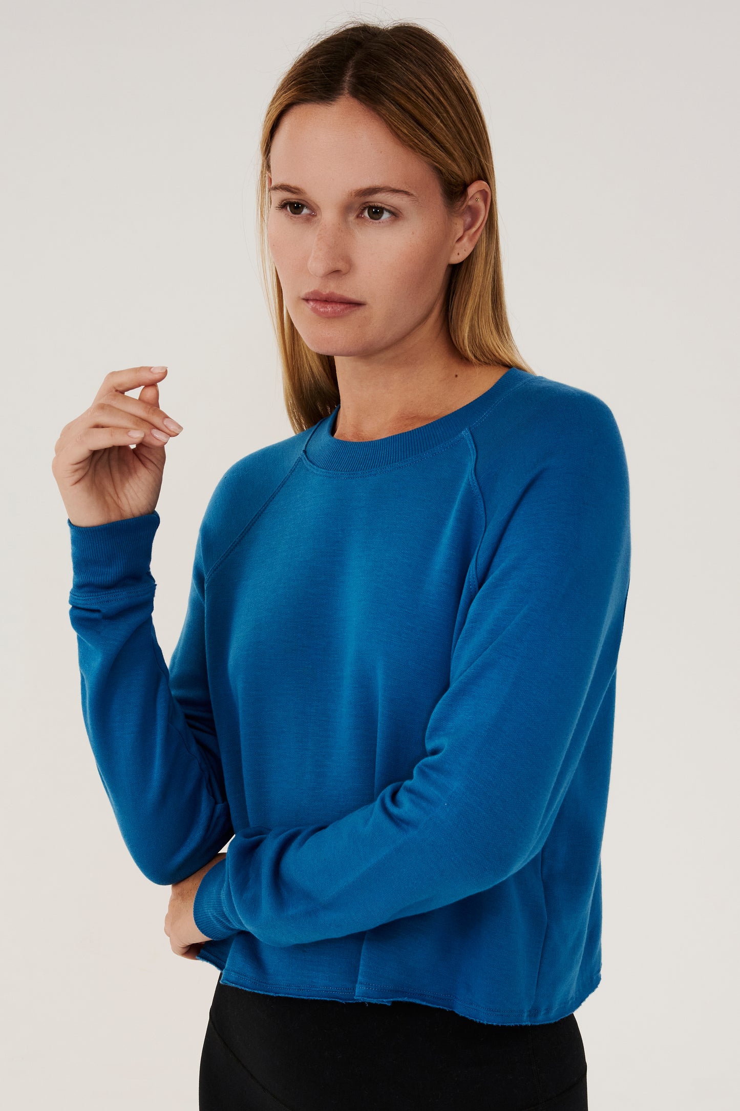 Front view of woman with dark blonde hair, wearing bright cropped blue sweatshirt with black leggings