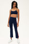 A woman wears the SPLITS59 Raquel High Waist Crop in Indigo/Pirate Red—navy with red side stripes—in 4-way stretch supplex, styled with white sneakers for yoga workouts, standing against a plain background.