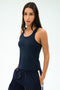A woman wears the SPLITS59 Mel Airweight Lite Tank in Indigo, paired with matching athletic pants, standing hands-in-pockets against a light background.