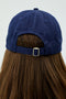 A person is seen from the back wearing a Tennis Cap - Indigo by SPLITS59, with long brown hair flowing beneath it.