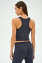 A woman in the Kiki Rib Crop Tank - Graphite by SPLITS59 and pants, made from soft baby rib fabric, is viewed from the back against a light background.