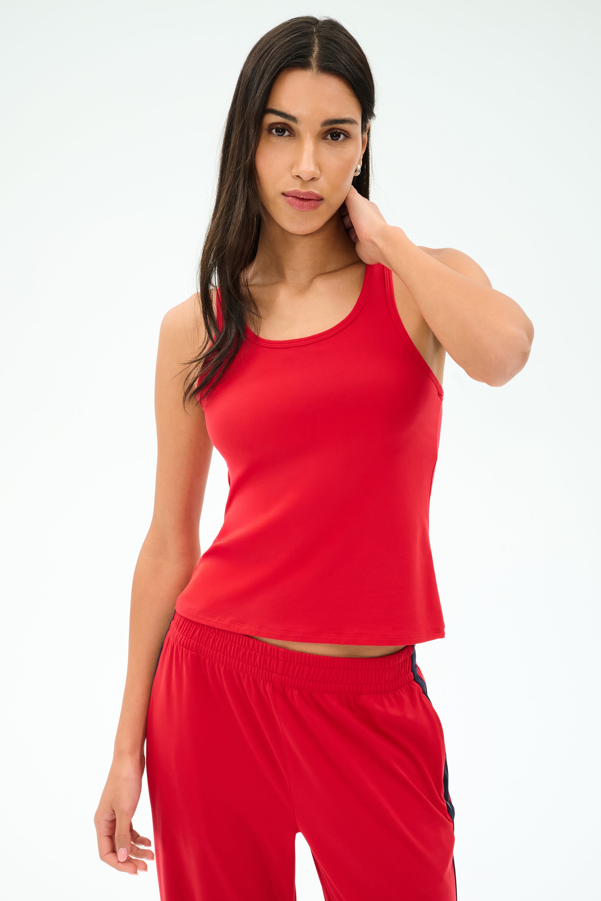 A woman models the SPLITS59 Mel Airweight Lite Tank in Pirate Red, standing against a plain white background with one hand behind her neck, looking at the camera.