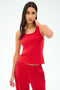 A woman models the SPLITS59 Mel Airweight Lite Tank in Pirate Red, standing against a plain white background with one hand behind her neck, looking at the camera.