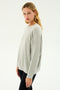 A person with long, blonde hair and a neutral expression is wearing the Andie Fleece Sweatshirt in Heather Grey by SPLITS59 and black leggings, posing against a plain white background.