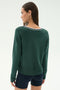 A woman stands with her back to the camera, wearing the SPLITS59 Sonja Fleece Sweatshirt W/ Stripe in Military—dark green soft modal with white and black collar trim—paired with black shorts.