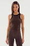 A woman with long hair wearing a sleeveless SPLITS59 Kiki Rib Crop Tank in Dark Chocolate/Black and brown pants stands against a plain background.
