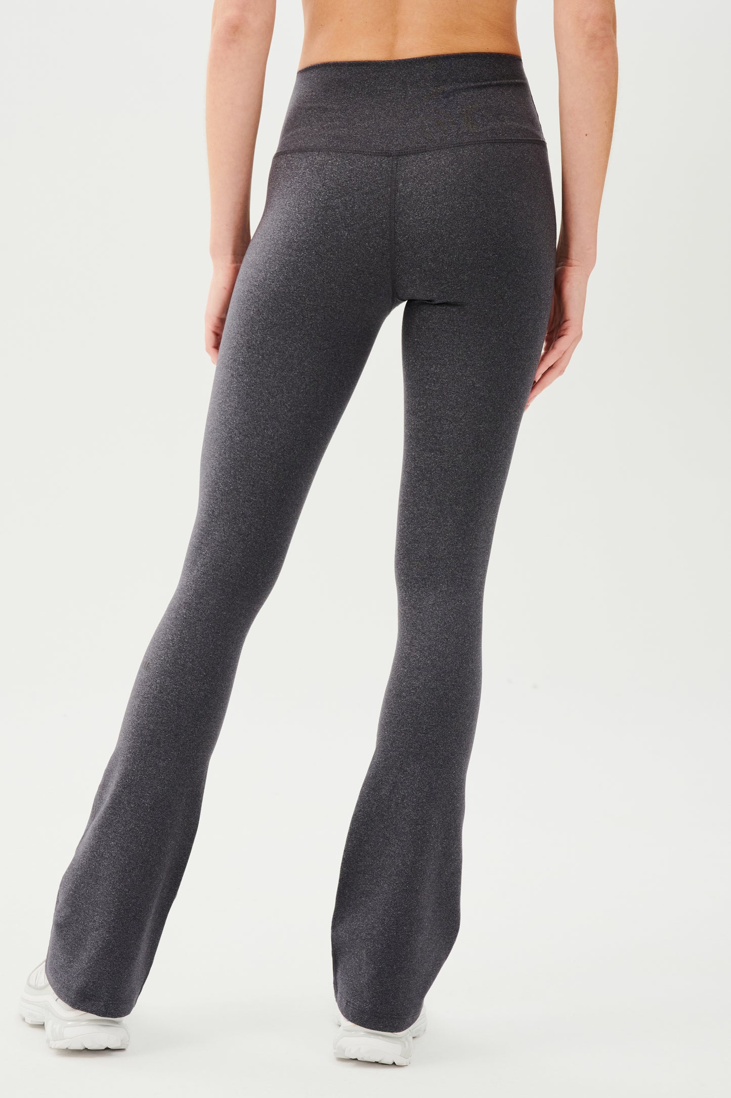 Back view of woman wearing dark gray high waist below ankle length legging with wide flared bottoms. Paired with white shoes.
