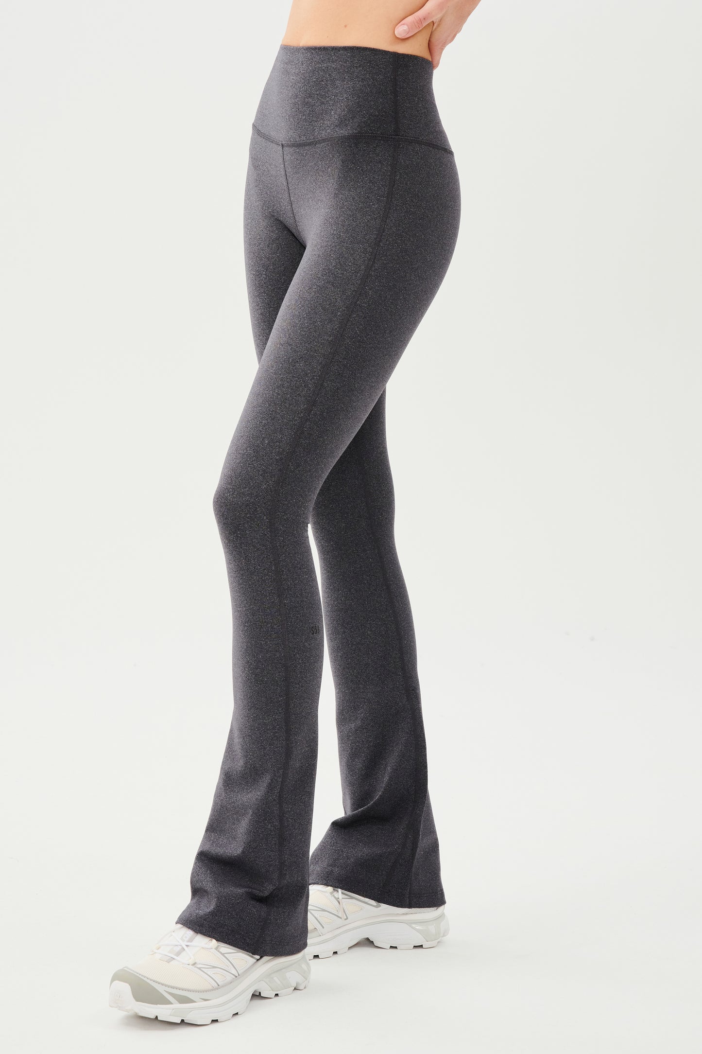 Front side view of woman wearing dark gray high waist below ankle length legging with wide flared bottoms. Paired with white shoes.