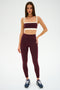 A woman wears the SPLITS59 Monah Rigor Bra in Dark Cherry/Creme, paired with matching high-waisted leggings and dark athletic shoes, standing against a plain white background.