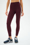 A person wearing SPLITS59 Clare High Waist Rigor 7/8 leggings in Dark Cherry/Creme with a white side stripe and navy New Balance sneakers, standing against a plain white background.