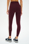 A person wears SPLITS59 Clare High Waist Rigor 7/8 leggings in Dark Cherry/Creme, accented with cream side stripes, paired with gray New Balance sneakers, standing against a plain white background.