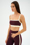 A woman models the SPLITS59 Monah Rigor Bra in Dark Cherry/Creme, a soft nylon-spandex workout set, standing against a plain white background and glancing to the side.