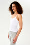 A woman wearing a SPLITS59 Loren Seamless Waist Length Tank in White with a shelf bra and grey sweatpants.