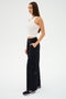 A person in a white sleeveless top and SPLITS59's Lucas Airweight Trouser - Black, made from ultra-luxe fabric, stands in profile with hands in pockets, showcasing sophisticated comfort against a plain background.