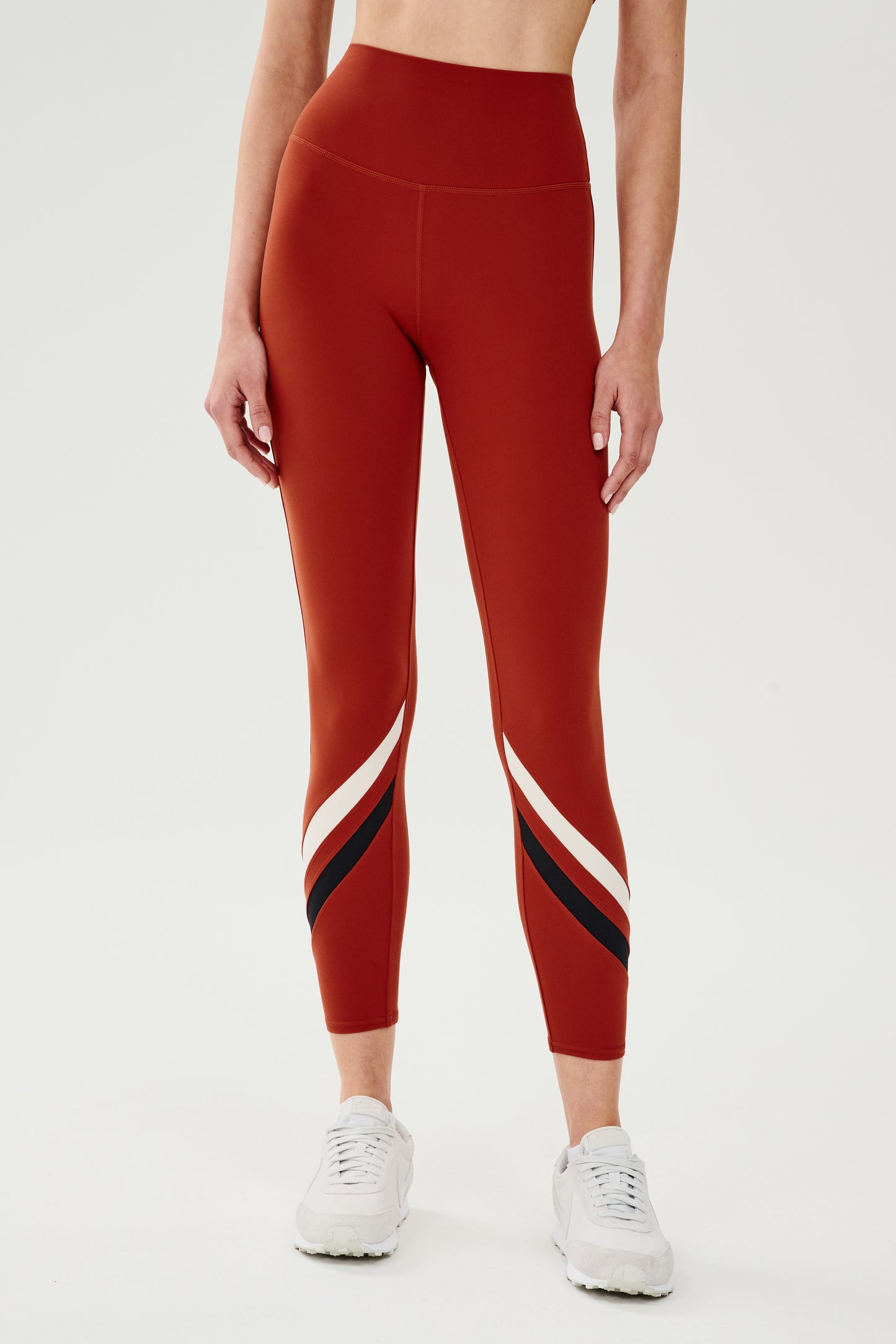 Front view of girl wearing red leggings with two white and black stripes across the shin white shoes