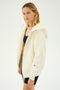 Dressed for Après-Ski, the individual wears the Lynx French Terry Sherpa Hoodie in Creme/Creme by SPLITS59, with its plush fleece lining offering cozy warmth over a black top and shorts, set against a plain white background. The craftsmanship of this MADE IN LOS ANGELES piece is evident in every stitch.