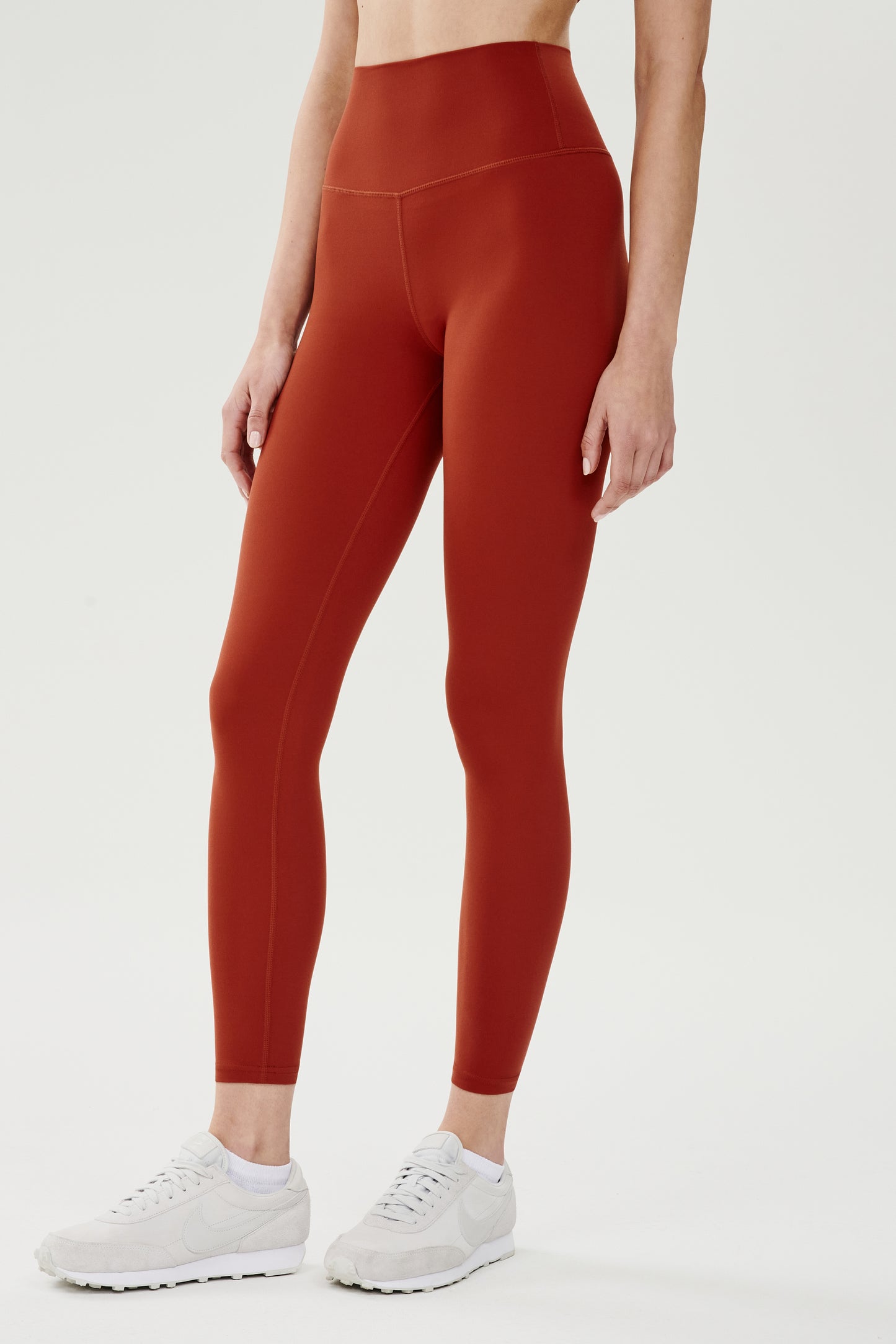 Side view of girl wearing highwasited dark orange leggings with white shoes