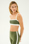 Woman in the SPLITS59 Monah Rigor Bra - Olive/White, looking to her left against a plain white background.