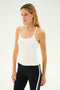 A woman with long blonde hair wearing the Airweight Tank in white by SPLITS59 and black leggings with a white stripe, perfect for hot yoga, stands against a plain background.