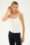 A person with long blonde hair, dressed in a white Airweight Tank by SPLITS59 and black leggings made from the same Airweight fabric, stands against a plain background with one hand touching their ear.